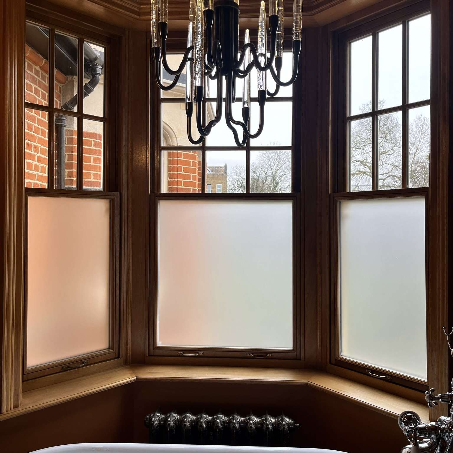Internal view of a high-end bathroom in Chigwell showing frosted window film applied to glazing, providing privacy while allowing natural light to pass through.