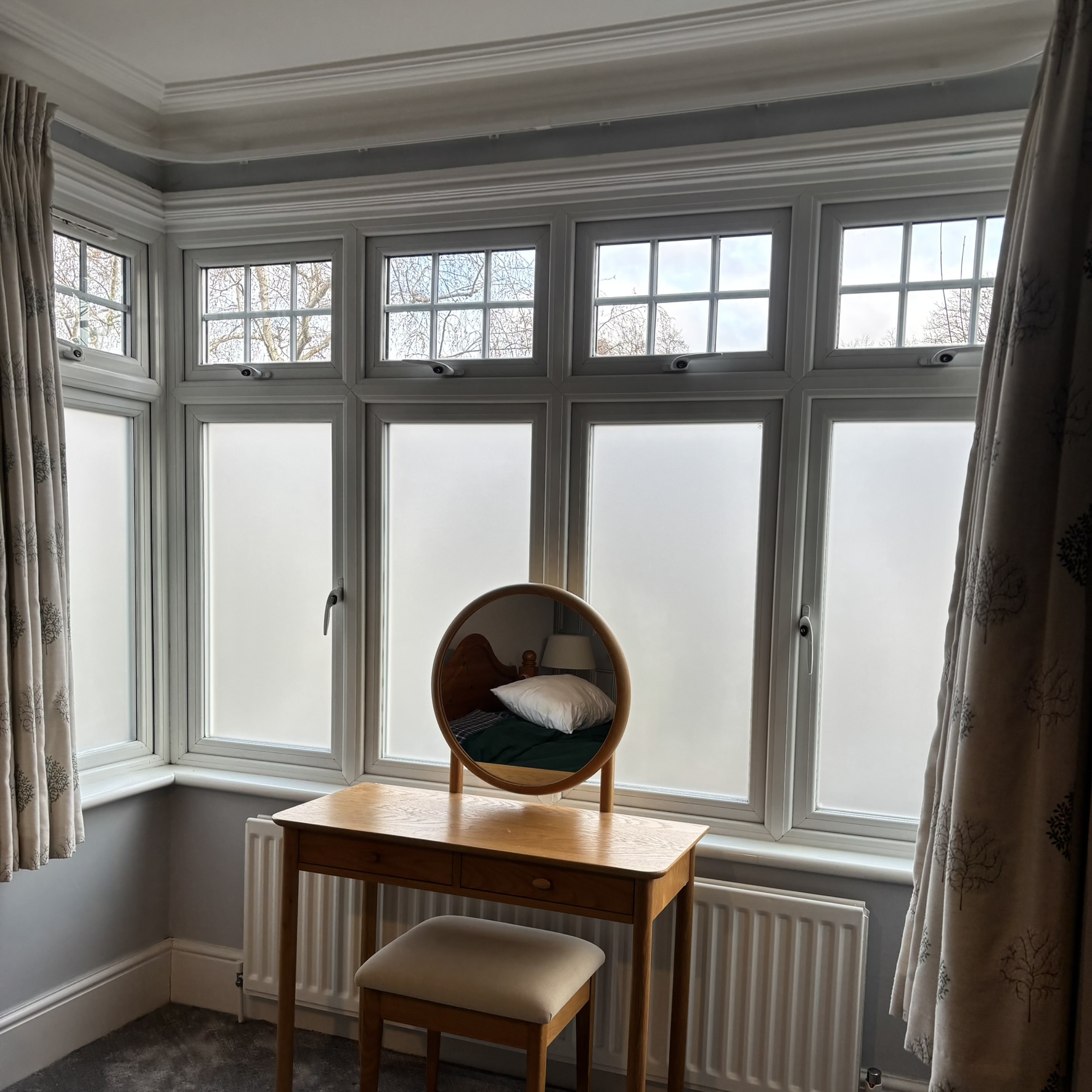 Interior view of a bedroom bay window in Hertford with frosted window film applied to the lower panes, providing 24-hour privacy while allowing natural light through and giving a clean, modern finish.