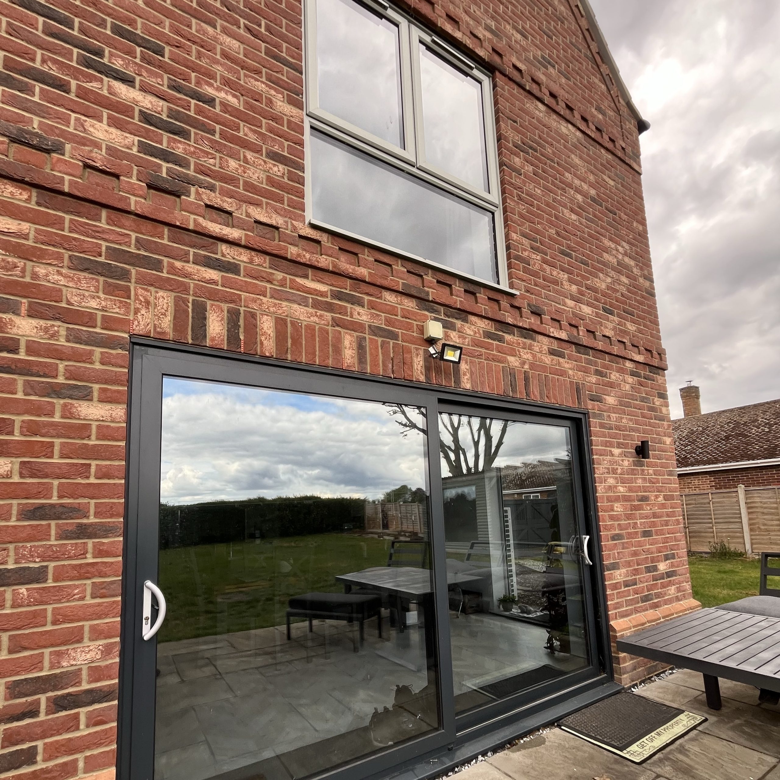 External rear view of a residential property in Thetford, Norfolk, with ground floor sliding doors fitted with Silver 50 reflective solar window film and an upstairs bedroom window fitted with Silver 20 for solar control and privacy.